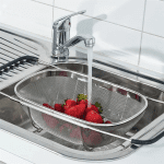 Expandable stainless steel sink colander basket used for rinsing produce and draining food over the kitchen sink